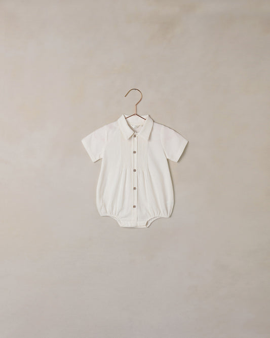 White baby romper on a hanger against a beige background